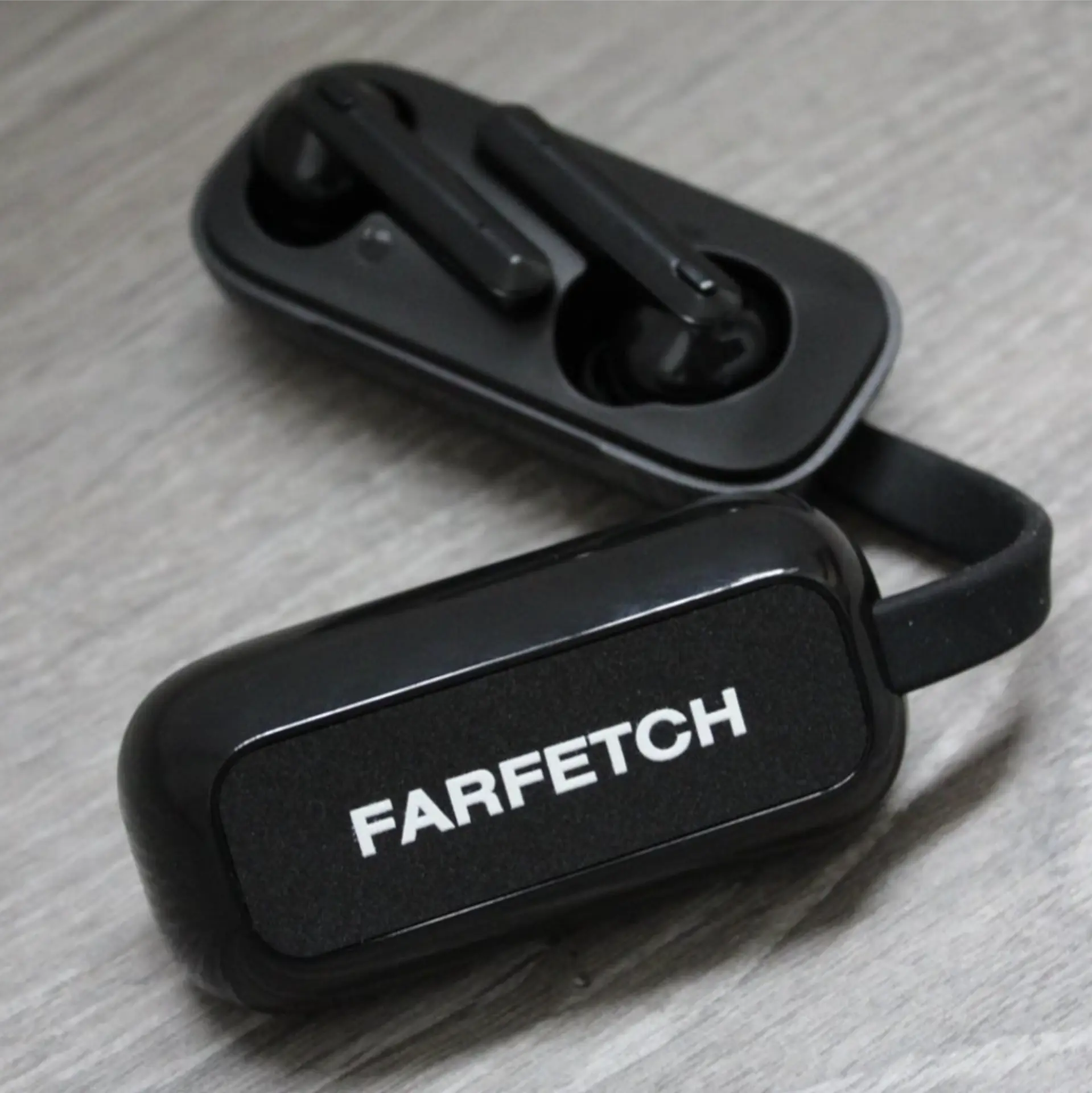 Black wireless earbuds in a charging case branded with the Farfetch logo