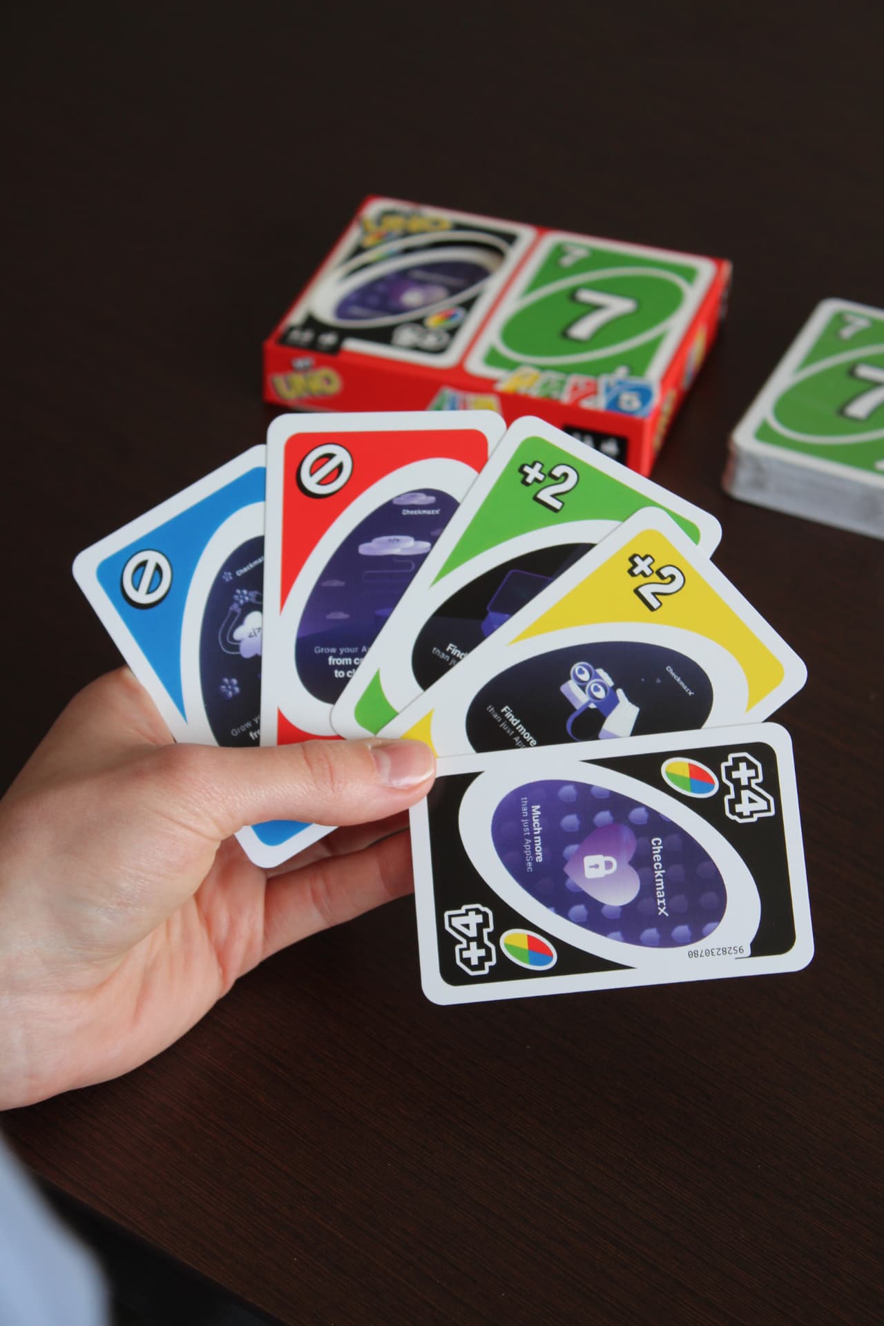 Hand of custom Checkmarx branded UNO playing cards with the printed box behind