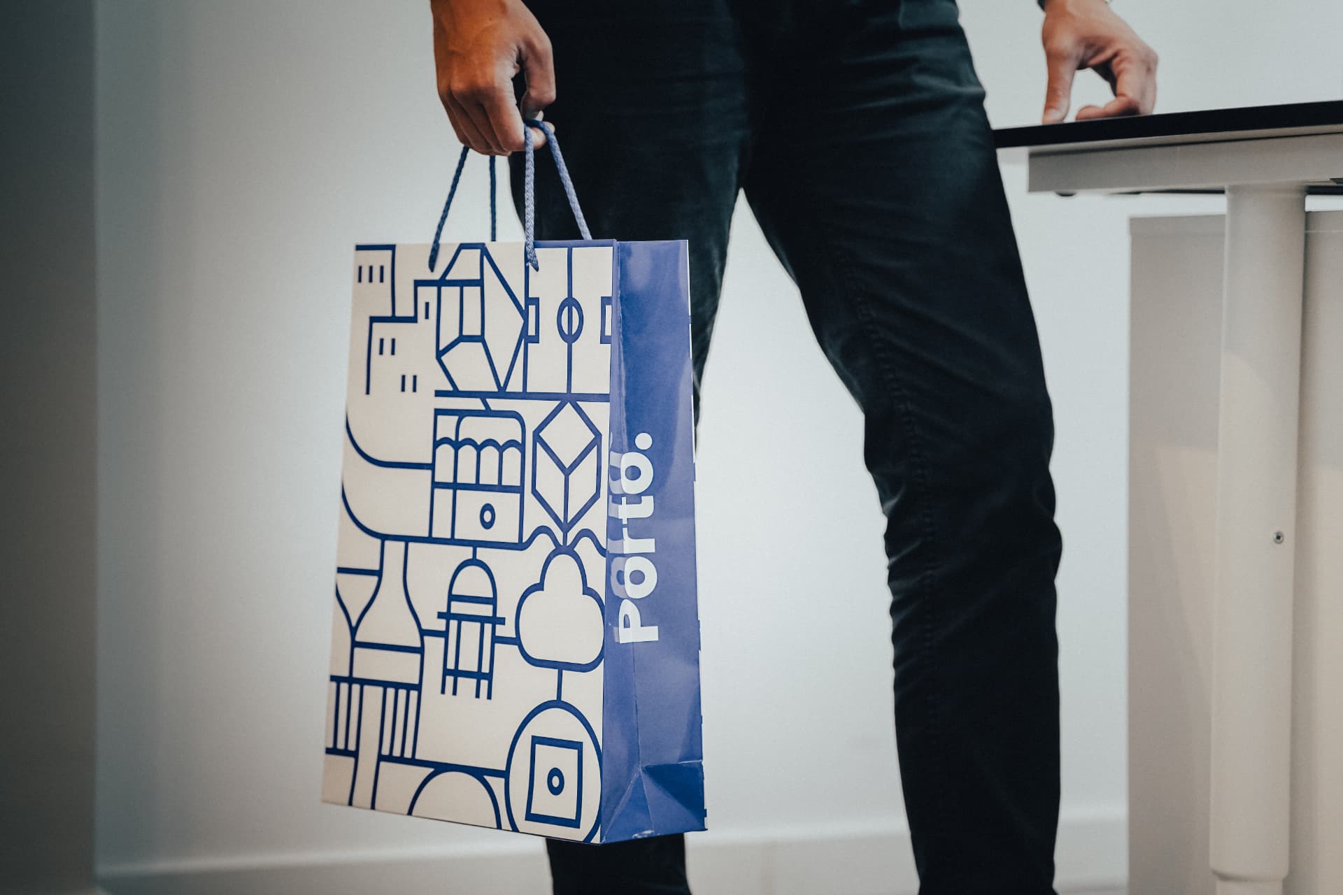 Person carrying a blue and cream illustrated Porto branded paper gift bag