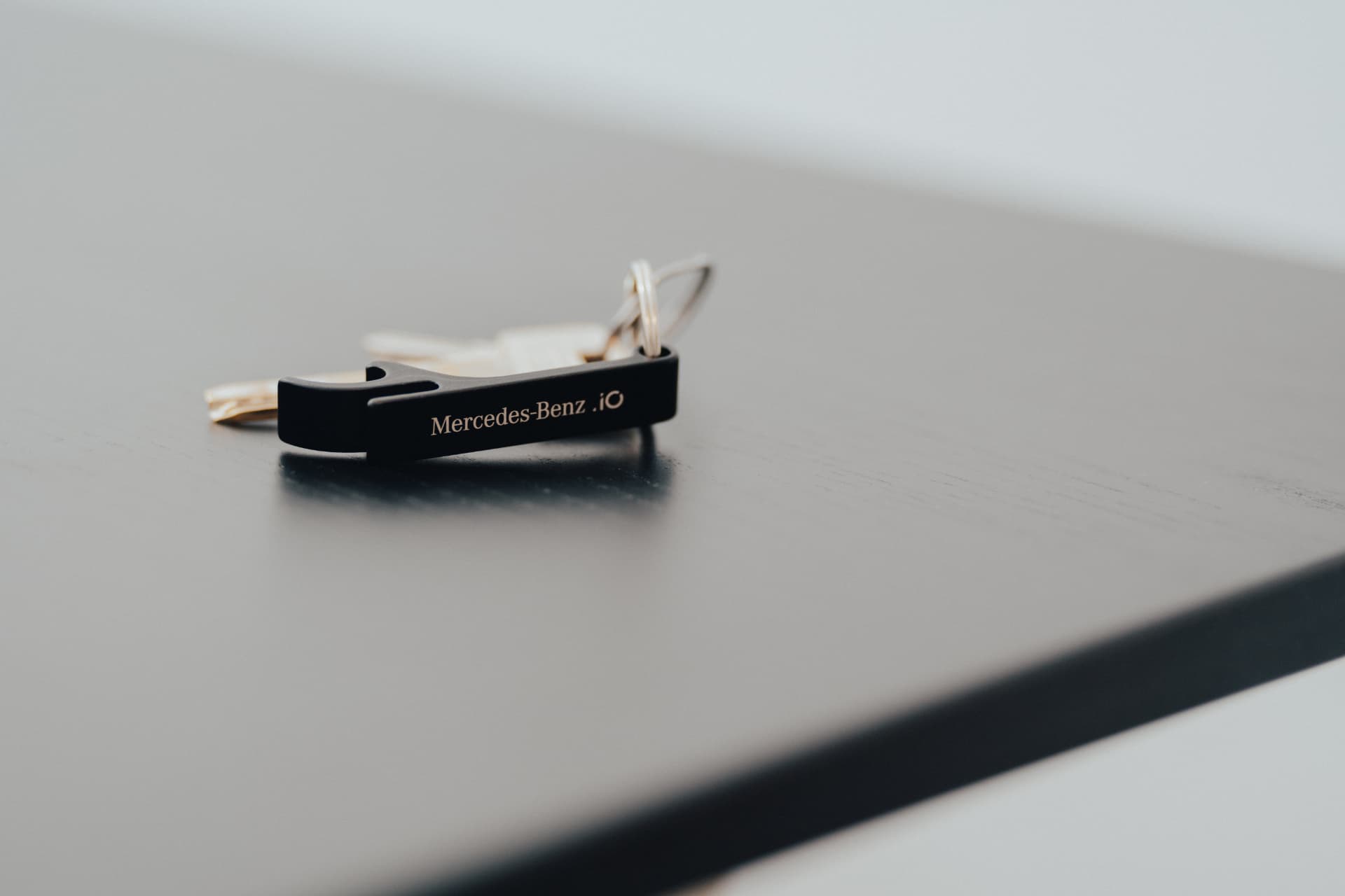 Matte black Mercedes-Benz.io engraved bottle-opener keyring on a dark desk