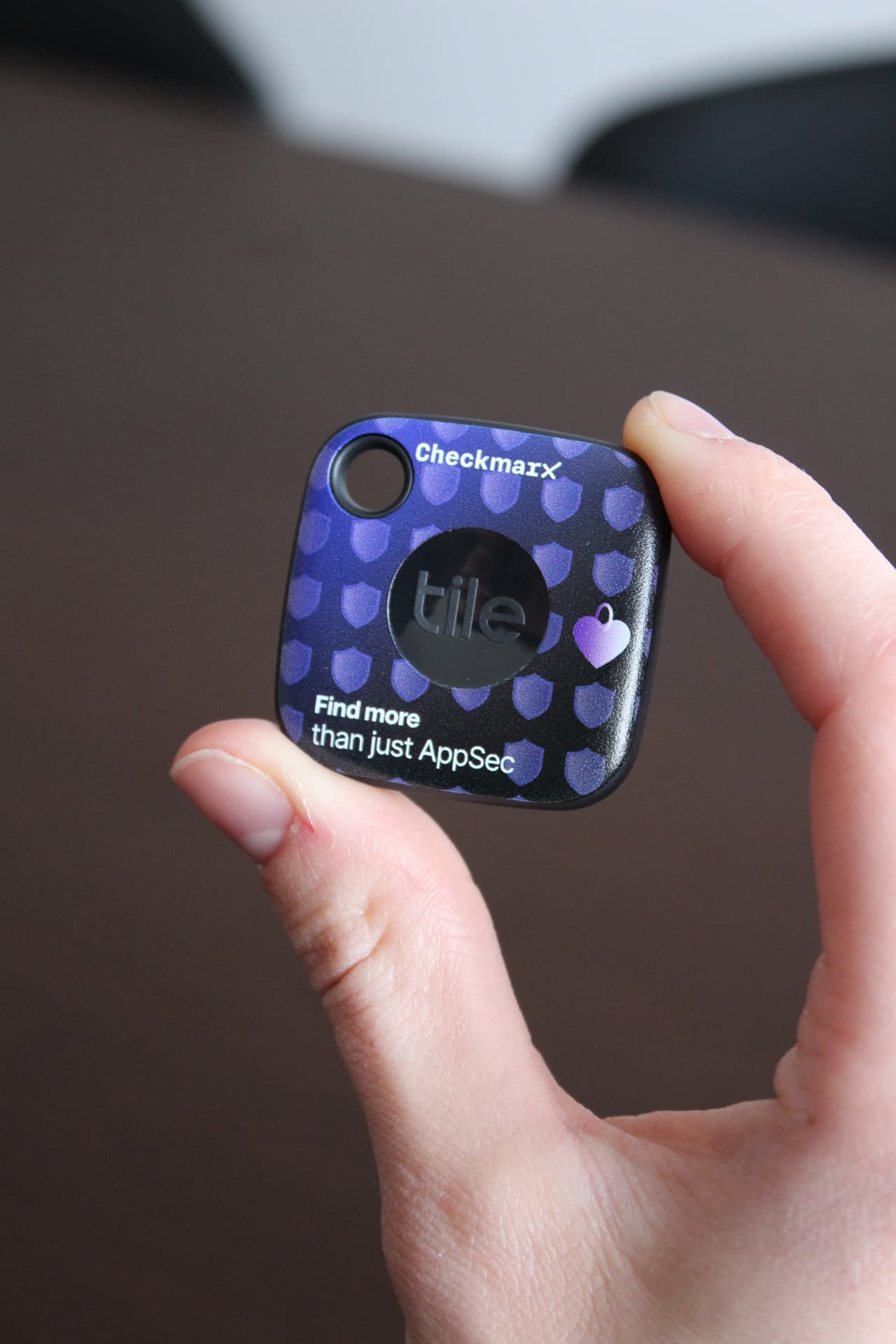 Hand holding a Checkmarx branded Tile bluetooth tracker keyring