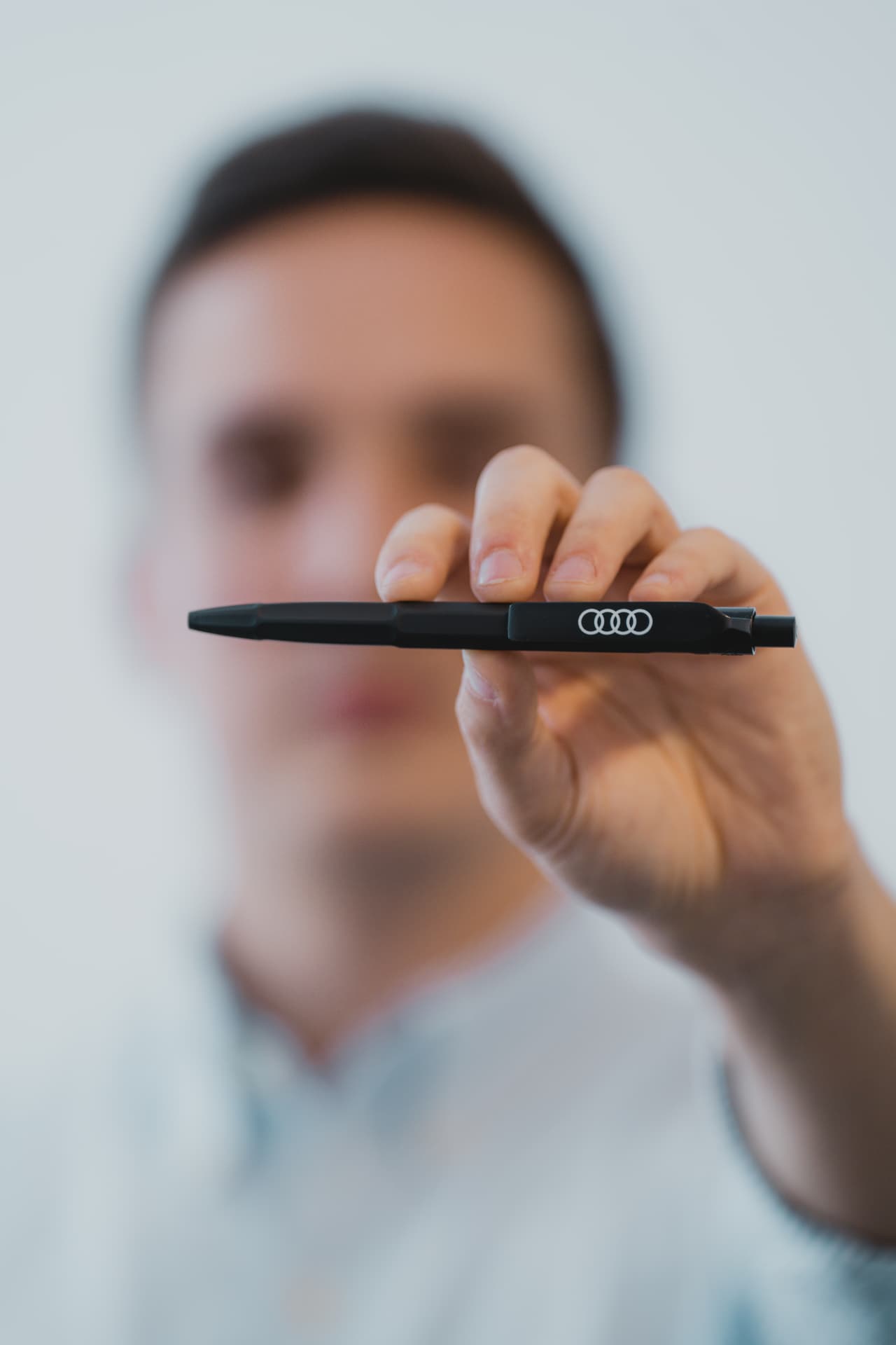 Hand holding a matte black ballpoint pen printed with the Audi rings logo